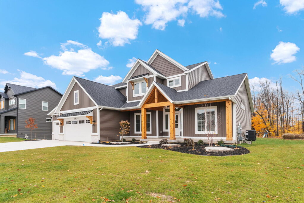 Front exterior of a gray two-story home with wood porch beams, white trim, attached garage, and a well-kept lawn.