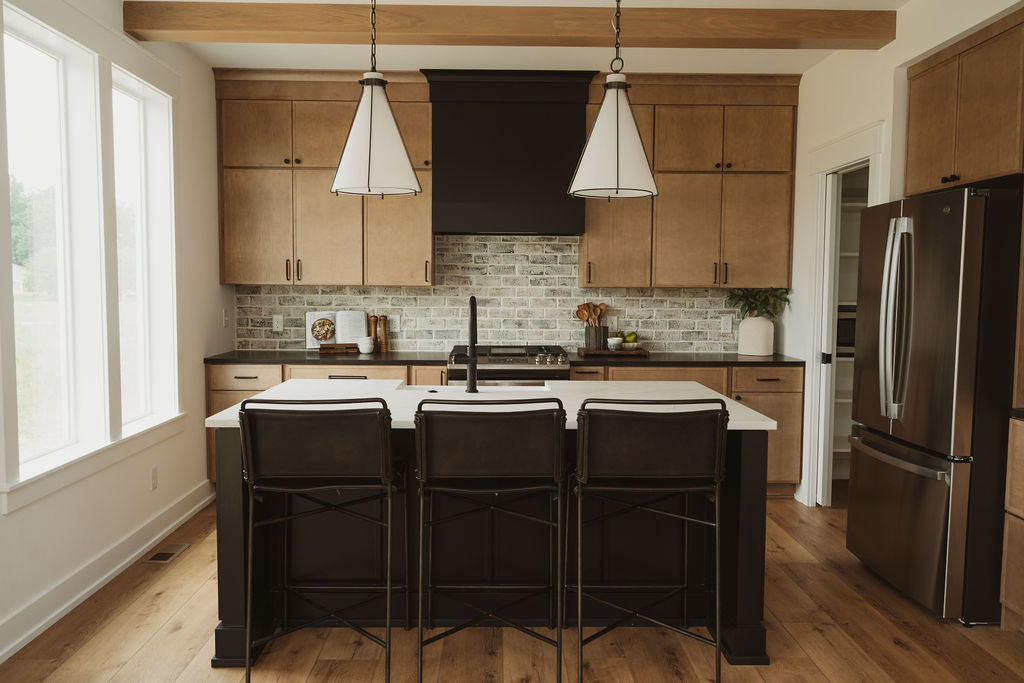 Kitchen with black island, wood cabinets, and pendant lights